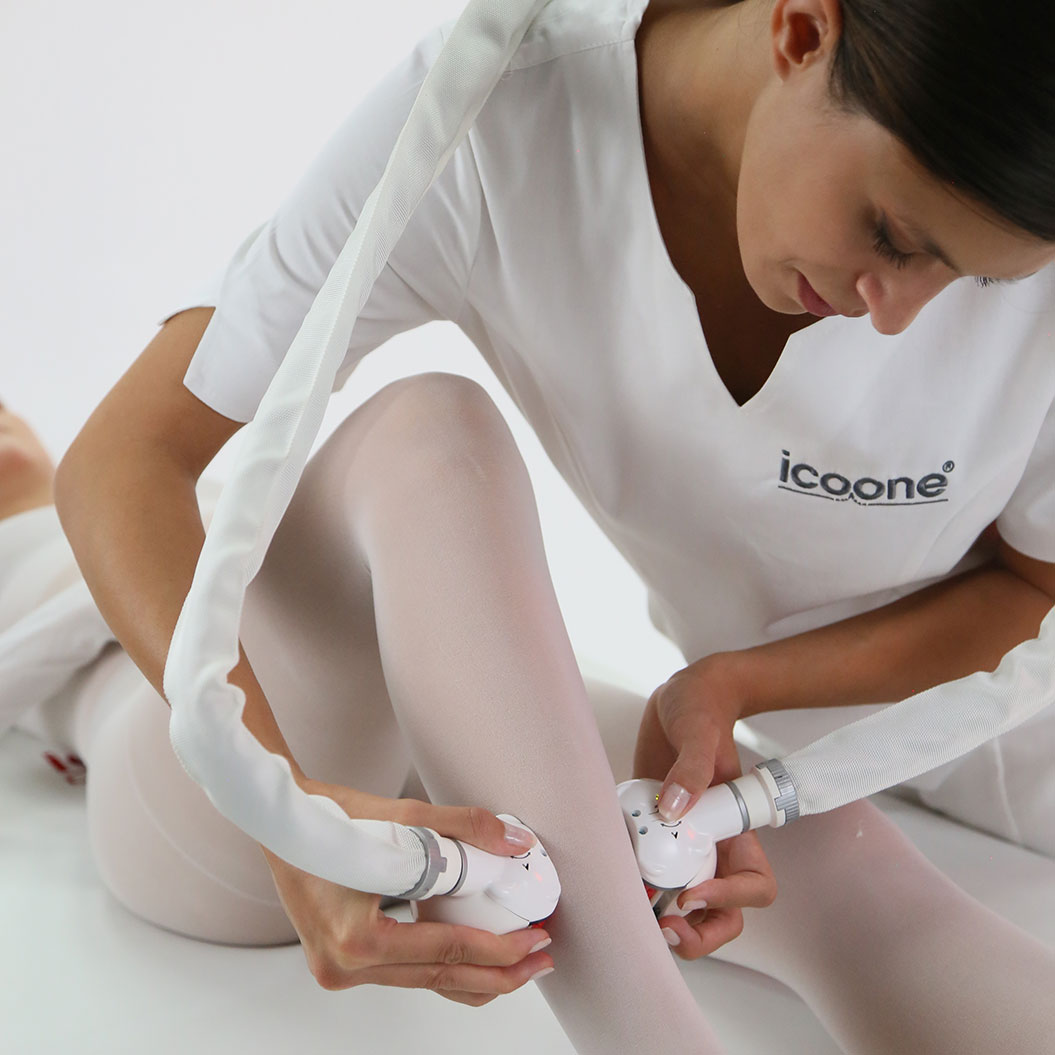 Eine Person in weißem Outfit führt eine Behandlung an Beinen mit Massagegerät durch, fokussiert.